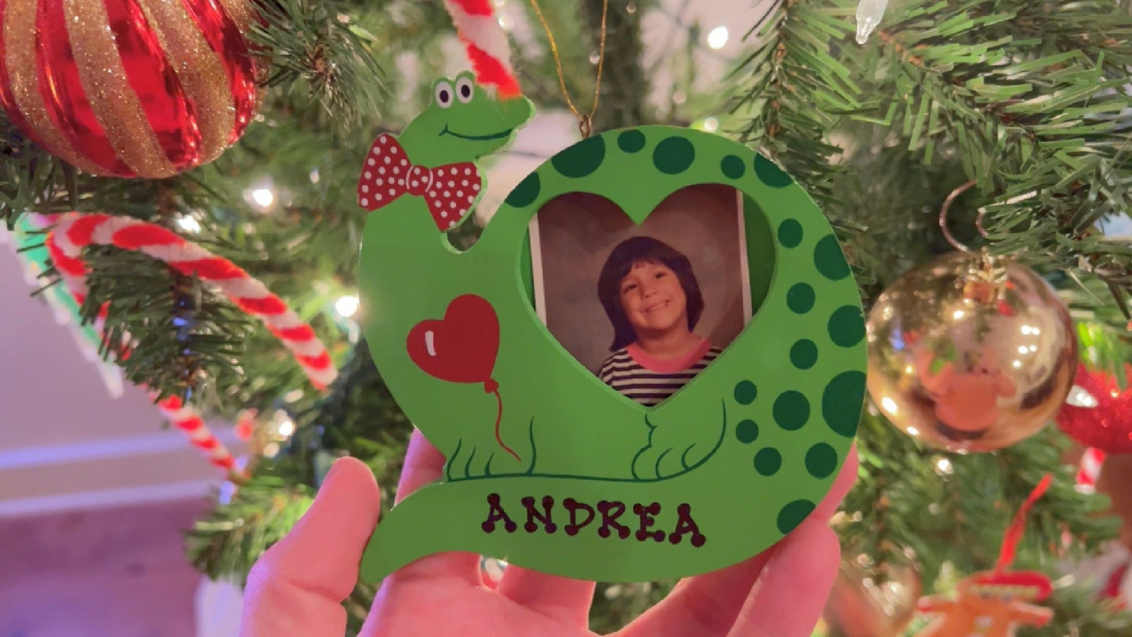 andrea valdez holding a christmas ornament that contains a photo of herself as a child